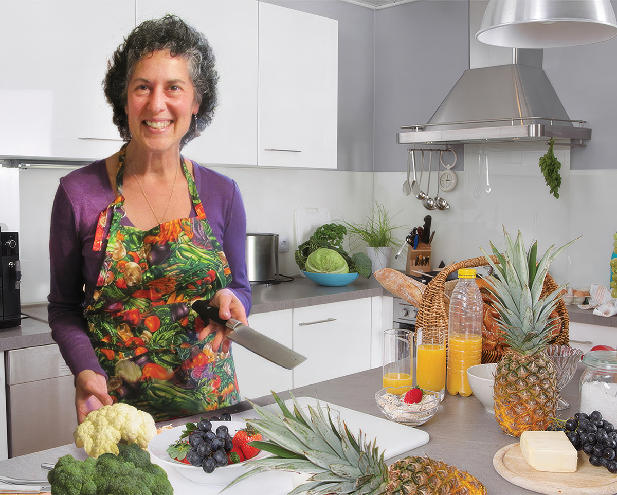 photo of Laurie Jacobson wearing colorful shirt and beaded necklace in a kitchen chopping vegetables